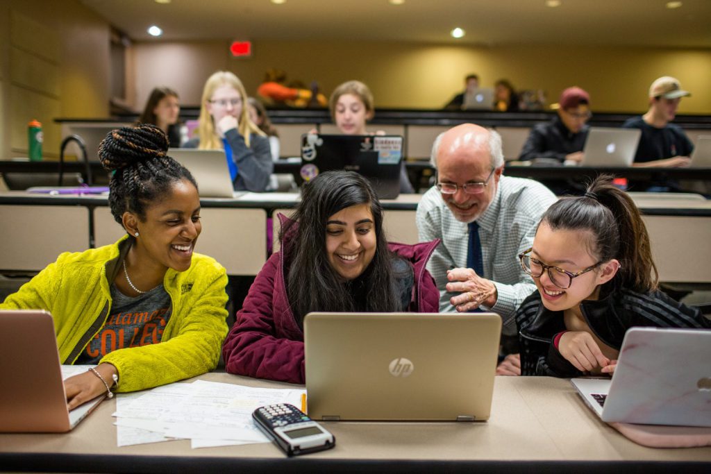 Students and a professor looking together at a laptop in class.
